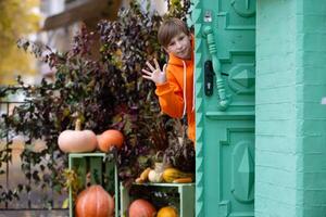 une garçon dans Orange vêtements regards en dehors de le porte de une maison décoré avec citrouilles pour Halloween. photo