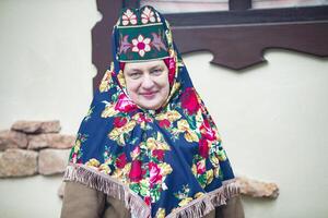 un personnes âgées russe femme dans une traditionnel coiffure, kokochnik, pose contre le toile de fond de une village maison. photo