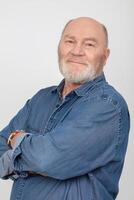 portrait de un attrayant et de bonne humeur aux cheveux gris homme dans une denim chemise isolé sur une gris Contexte. photo