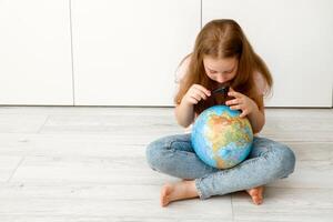 peu fille soigneusement examine le globe par une grossissant verre photo