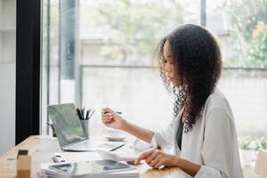 femme d'affaires est engagé dans en train de lire les documents avec une réfléchi expression, avec sa portable ouvert dans une brillant Bureau paramètre. photo