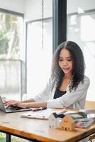 professionnel réel biens agent est concentré sur sa portable avec maison des modèles et les documents sur le bureau, dans une brillant bureau. photo