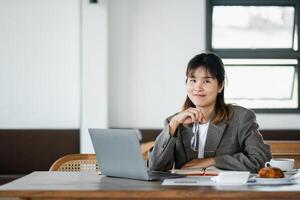 souriant Jeune entrepreneur avec une pensif expression des plans sa journée à une café, portable ouvert et petit déjeuner sur le tableau, prêt pour productivité. photo