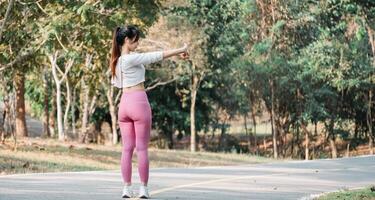 aptitude passionné prépare pour une faire du jogging par élongation sa bras sur une tranquille route entouré par le calme de la nature. photo