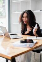 femme d'affaires sourit tandis que en utilisant une calculatrice à sa bureau avec une portable ouvert. photo