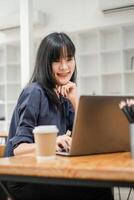 réfléchi femme d'affaires dans marine bleu chemise travail sur sa portable avec une café tasse et des crayons sur le bureau. photo