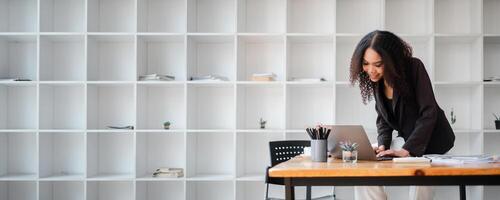 femme d'affaires dans une foncé blazer travaux intensément sur une portable à une moderne Bureau bureau. photo