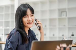 femme d'affaires avec un appareil dentaire sourit tandis que parlant sur le téléphone, portable ouvert dans de face de sa dans une brillant Bureau environnement. photo