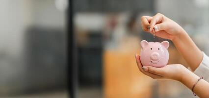 mains insertion une pièce de monnaie dans une rose porcin banque, symbolisant le concept de des économies et financier responsabilité. photo