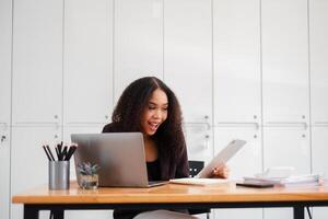 joyeux femme d'affaires est surpris comme elle lit positif nouvelles sur sa tablette à sa espace de travail, avec une portable et Stationnaire sur sa bureau. photo