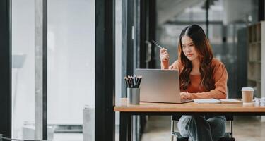 introspectif femme d'affaires envisage sa travail, stylo dans main, tandis que séance à sa portable dans une Bien organisé Bureau espace. photo