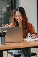 joyeux Jeune femme engageant dans une appel, en portant une stylo et avec une carnet sur sa bureau, dans une brillant moderne bureau. photo