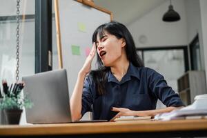 une femme est séance à une bureau avec une portable et une tableau blanc derrière sa photo