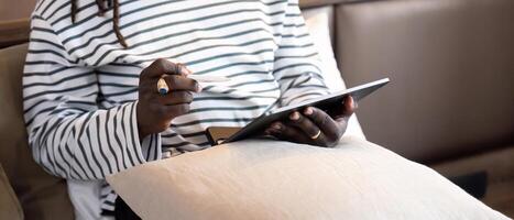 souriant Jeune africain américain homme en utilisant numérique tablette éloigné emploi séance sur le lit à maison. concept en ligne La technologie la communication photo