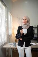 affaires femme musulman. sur de soi femme d'affaires musulman dans hijab permanent avec Matin café agresser dans Bureau photo