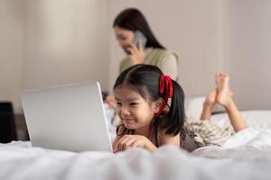 asiatique content Jeune mère et bébé mode de vie travail sur ordinateur portable, mère travail sur lit avec fille apprentissage La technologie sur portable ordinateur sur chambre lit photo