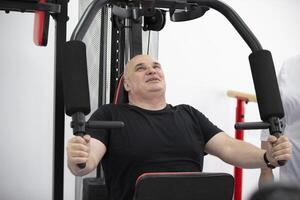 un personnes âgées homme travaux en dehors sur une des sports machine, pompage en haut le sien bras muscles. photo