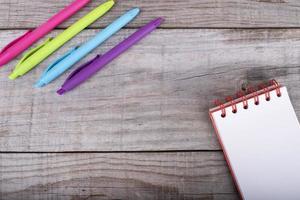 bloc-notes avec des feuilles blanches et un ensemble de stylos de couleur sur fond de bois photo