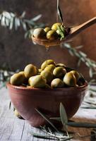 verser de l'huile sur une cuillère en bois avec des olives sur un bol rempli photo