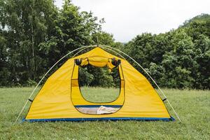 une Jaune Cadre tente des stands dans une clairière contre le Contexte de le forêt, un ouvert entrée à le tente, non personnes, randonnée équipement, métal arcs, un interne store. photo