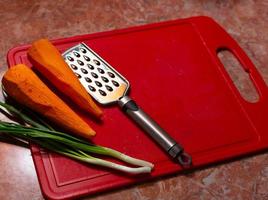 oignon vert, carotte, râpe sur planche de cuisine vintage en plastique rouge. photo