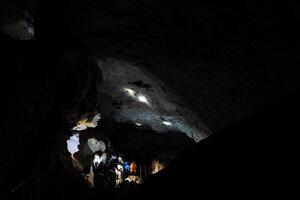 souterrain karst la grotte une groupe de gens inspecter le coffres de le ancien habitation de une Homme des cavernes, touristes Aller sur excursions souterrain, le lumière de le lampe frontale. photo