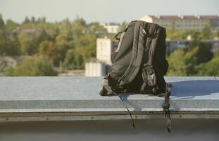 sac à dos noir se trouve sur la bordure métallique du toit de l'immeuble résidentiel à plusieurs étages par temps ensoleillé photo