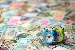 petit alarme l'horloge sur beaucoup billets de banque de différent monnaie. Contexte de temps et argent photo