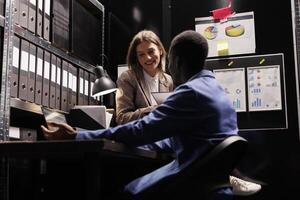 diverse équipe en cours d'analyse la gestion recherche, travail en retard à nuit à bureaucratie record dans espace de rangement chambre. hommes d'affaires dans formel costume vérification administratif les documents dans entreprise dépôt. photo