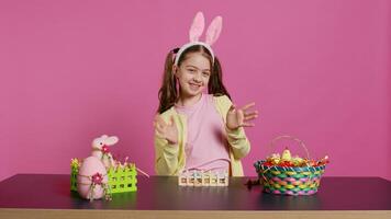 joyeux enfant en mettant lapin oreilles sur sa tête et agitant à caméra, en disant Bonjour et souriant dans excitation pour le Pâques vacances. content bambin ayant amusement avec art et artisanat activité. caméra b. photo