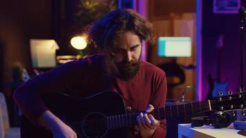 Jeune homme en jouant guitare et création la musique en utilisant égaliseur choucas Logiciel interface. la musique producteur enregistrement chanson dans Accueil studio et mélange acoustique des sons sur stéréo console. caméra un. photo