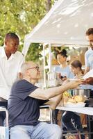 charitable équipe des offres Aidez-moi à le dépourvu et distribue gratuit nourriture comprenant Frais des fruits à sans-abri. une en fauteuil roulant désactivée individuel aussi reçoit faim allégement assistance. photo