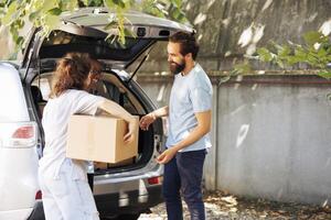 image montrant pauvres et Moins privilégié caucasien femme recevoir don boîte de Multi-éthnique bénévoles à nourriture conduire. Jeune charité ouvriers fournir essentiel articles à le nécessiteux et sans abri personnes. photo