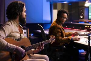 Jeune chanteur compositeur création une Nouveau Piste sur guitare dans enregistrement studio, du son designer écoute à la musique avant mélange Beats sur l'audio console. qualifié artiste composition Chansons dans contrôle chambre. photo