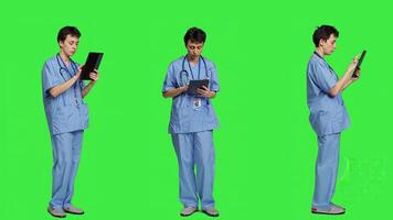 médical assistant navigation en ligne les pages Web sur tablette et SMS, en utilisant social médias applications à bavarder avec personnes. infirmière navigue l'Internet sur gadget, permanent contre écran vert toile de fond. caméra un. photo