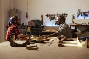 menuisier et bipoc collaborateur en utilisant cad Logiciel sur portable à conception en bois objets. Charpentier et africain américain homme en utilisant programme sur carnet à plan meubles assemblage dans menuiserie photo