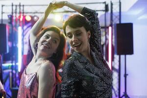 de bonne humeur copines improvisation se déplace sur piste de dance, célébrer et faire la fête dans boîte de nuit. Jeune insouciant femmes copains dansant et ayant amusement à discothèque un événement dans club photo