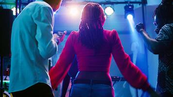 Hommes et femmes dansant à boîte de nuit et écoute à musique, ayant amusement à club avec étape lumières. groupe de les personnes profiter social rassemblement avec copains sur Danse sol. ordinateur de poche tir. photo