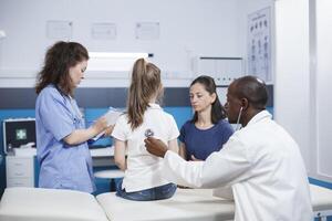 à vérification, médecin écoute à battement de coeur de enfant en utilisant stéthoscope. médical rendez-vous dans soins de santé bureau, général praticien examine santé de Jeune fille avec assistance de une femelle infirmière. photo