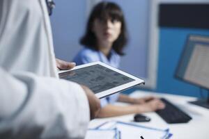 sélectif concentrer sur un individuel portant une blanc laboratoire manteau saisir une tablette tandis que une infirmière les usages une bureau pc. fermer coup de soins de santé ouvriers révision médical Les données par en utilisant moderne technologie. photo