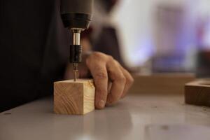 menuisier dans Assemblée magasin en utilisant Puissance percer à créer des trous pour chevilles dans en bois planche. Charpentier naufrage des vis dans en bois surfaces avec électrique outil, Faire précis forage pour sans couture menuiserie photo