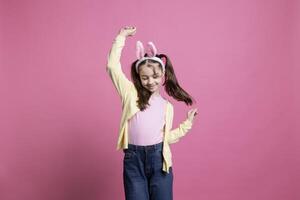 énergique et positif enfant dansant dans studio tandis que portant lapin oreilles dans excitation de Pâques dimanche célébrations. heureux insouciant enfant qui affiche confort dans sa Danse compétences. photo