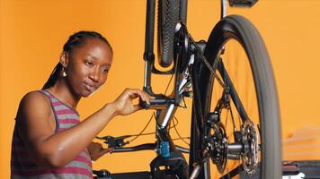 de bonne humeur technicien vérification vélo performance par filage pédales. souriant expert assurer correct une fonction de pneus sur bicyclette roues dans Orange studio Contexte pendant vérification, caméra une photo