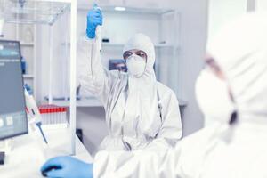 laboratoire scientifique dans soins de santé laboratoire en portant micropipette avec échantillon habillé dans ppe costume contre corona virus. équipe de microbiologistes dans recherche laboratoire conduite expérience pendant global pandémie avec COVID-19 [feminine. photo