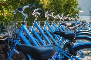 bleu Vélos soigneusement amarré à bicyclette partage gare, Urbain paramètre, vert feuillage Contexte. photo