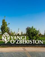 Ouzbékistan, Tachkent - septembre 15, 2023 une inscription Yangi Ouzbékistan et monument de indépendance dans le forme de une stèle avec une humo oiseau sur une jour dans le Nouveau Ouzbékistan parc dans été. photo