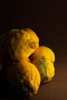 une grappe de grand, texturé citrons repose sur une rustique marron Contexte. le vibrant Jaune de le citrons les contrastes avec le terreux tons, mise en évidence leur unique rugueux peau et Naturel apparence. photo