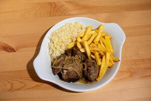 une assiette de cuit noir porc joues, jumelé avec blanc riz et croustillant français frites, affiché dans une restaurant paramètre. cette traditionnel Portugais plat est une chaud et copieux repas photo