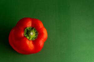 une brillant rouge poivre est assis contre une vert toile de fond, création une vif Couleur contraste. le image points forts le poivrons lisse texture et riches teinte, suggérant fraîcheur et dynamisme. photo