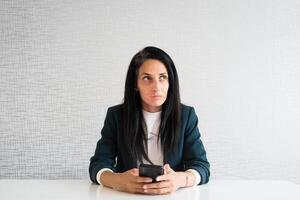 jeune caucasien brunette femme d'affaires directeur au bureau entrepreneur réfléchi tenir le téléphone prendre des décisions penser avant le texte r maquette isolé photo